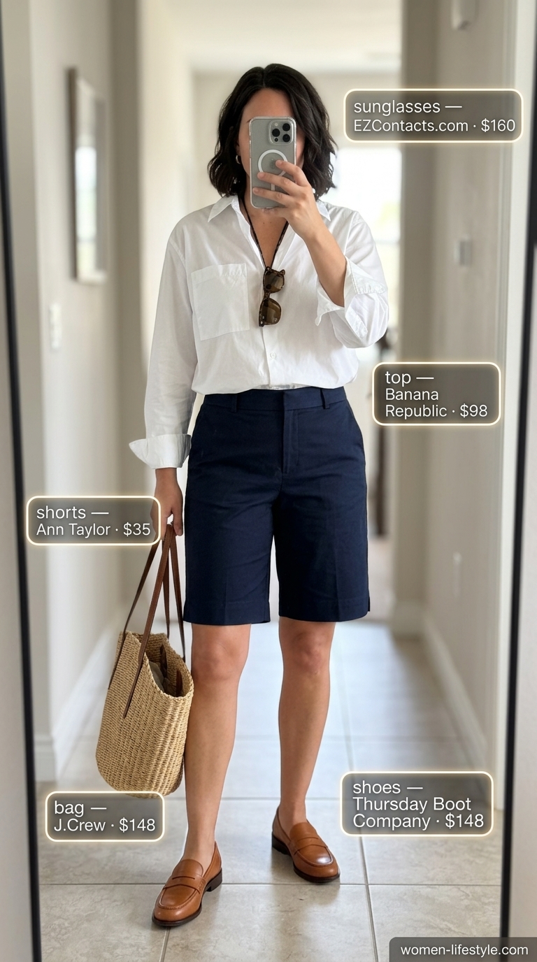 Tailored quiet luxury summer outfit: Navy Bermuda shorts, crisp white shirt, tan loafers, straw tote. Modern prep style.