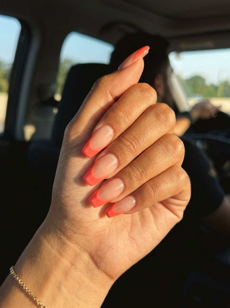 Coral Smile Line: Bold vacation nails summer 2026 with vibrant coral reverse French on nude coffin nails.