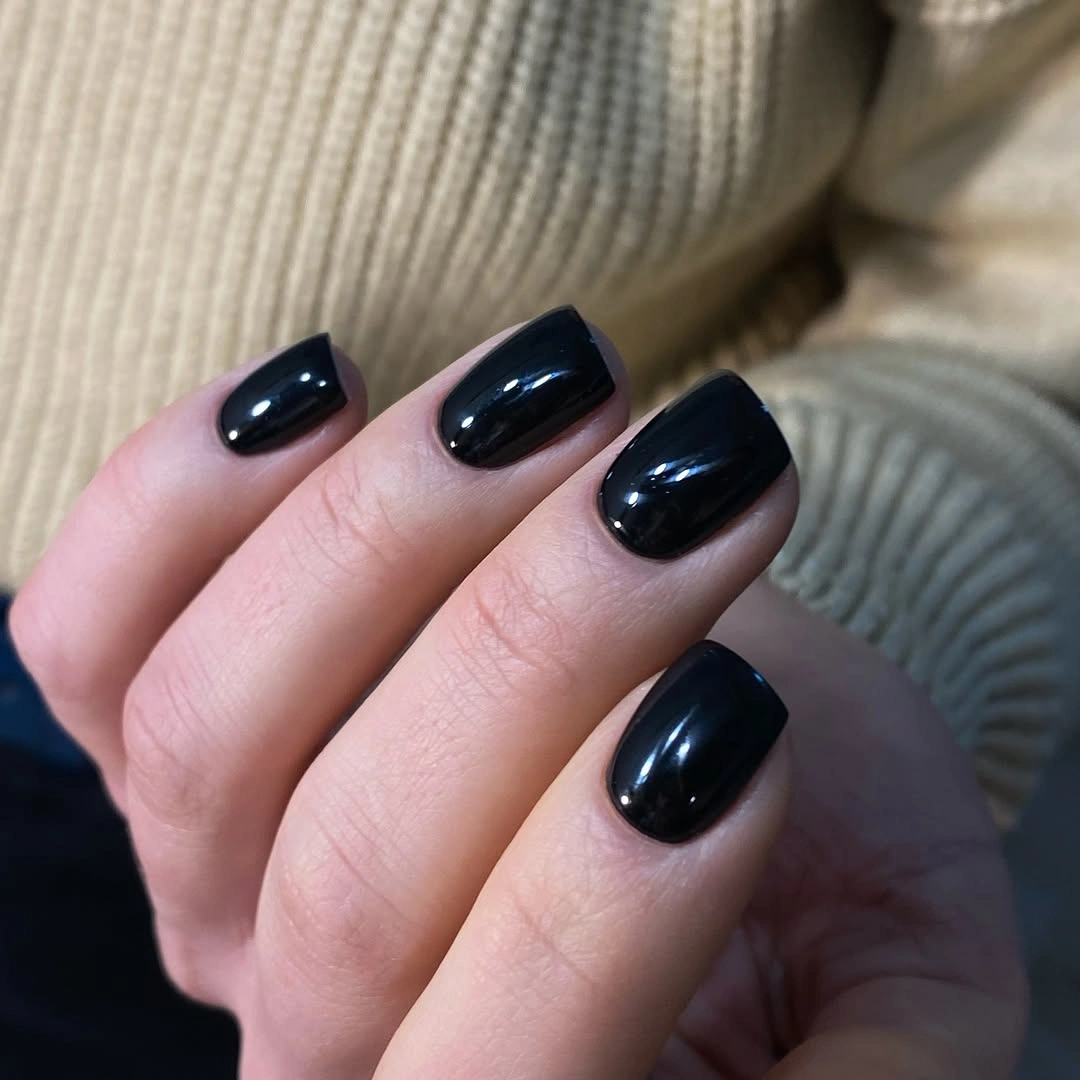 Short glossy black nails beside a cream knit sleeve