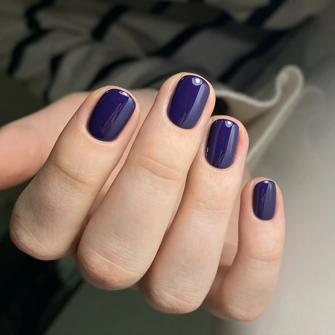 Short glossy inky violet nails in a rounded-square shape