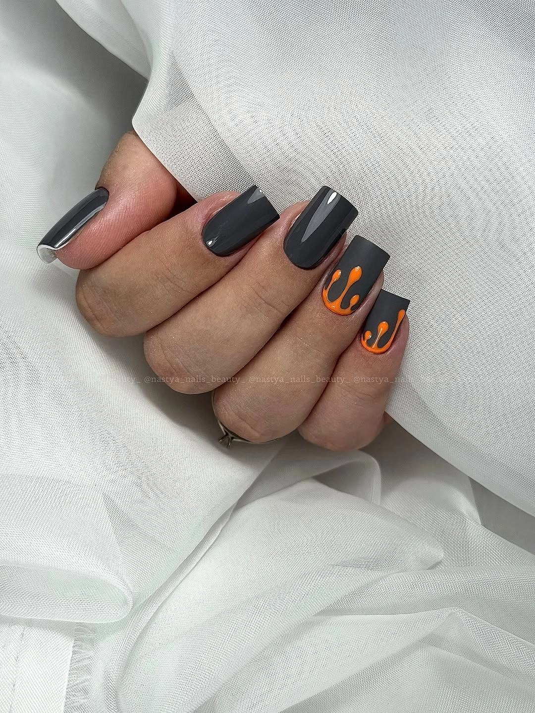 Short charcoal nails with bright orange curved accents
