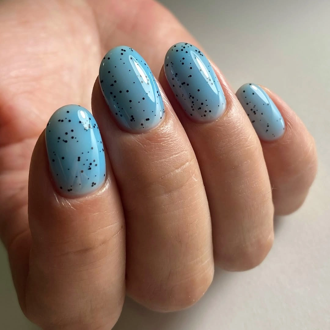 Short powder blue nails with scattered dark speckles