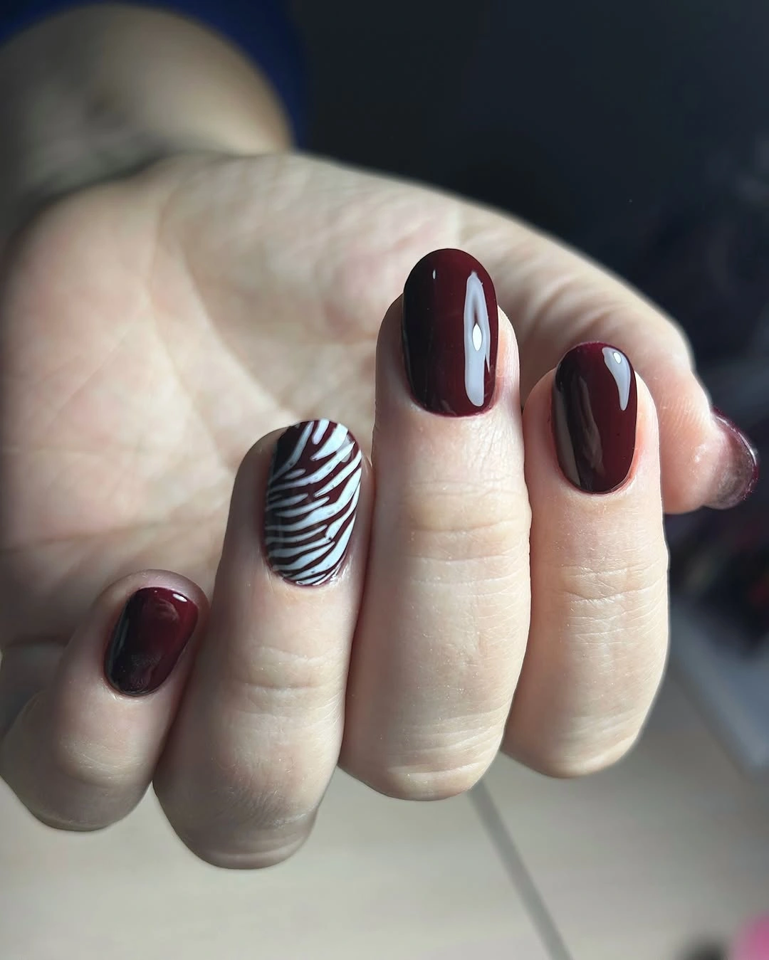 Short burgundy nails with one wavy black white accent nail