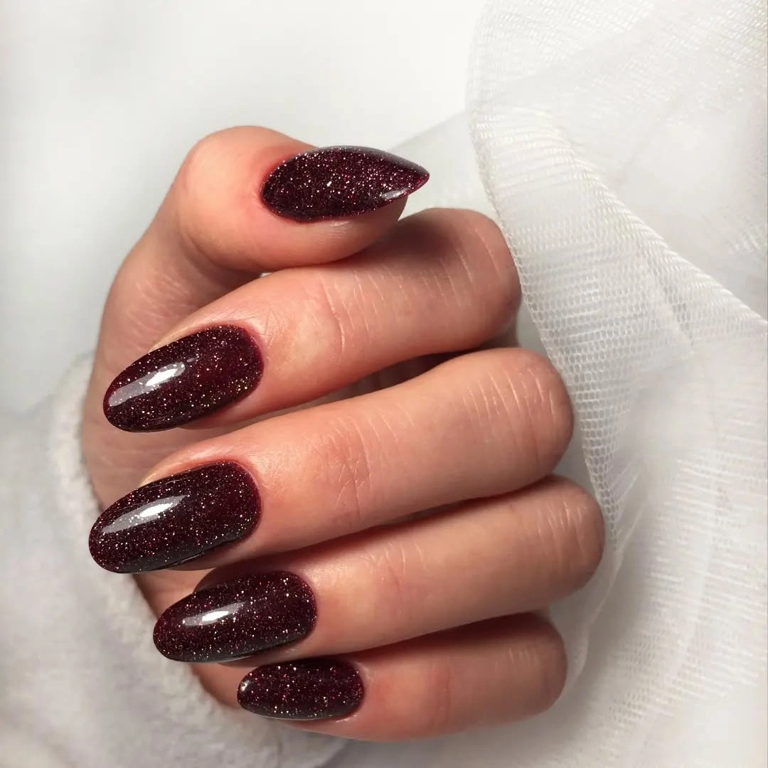 Long burgundy almond nails covered with fine red sparkle