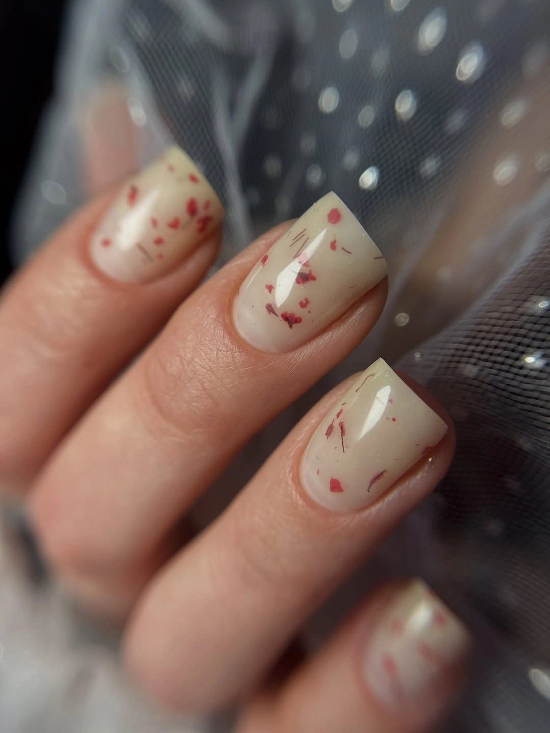 Short cream nails with scattered irregular red fragments