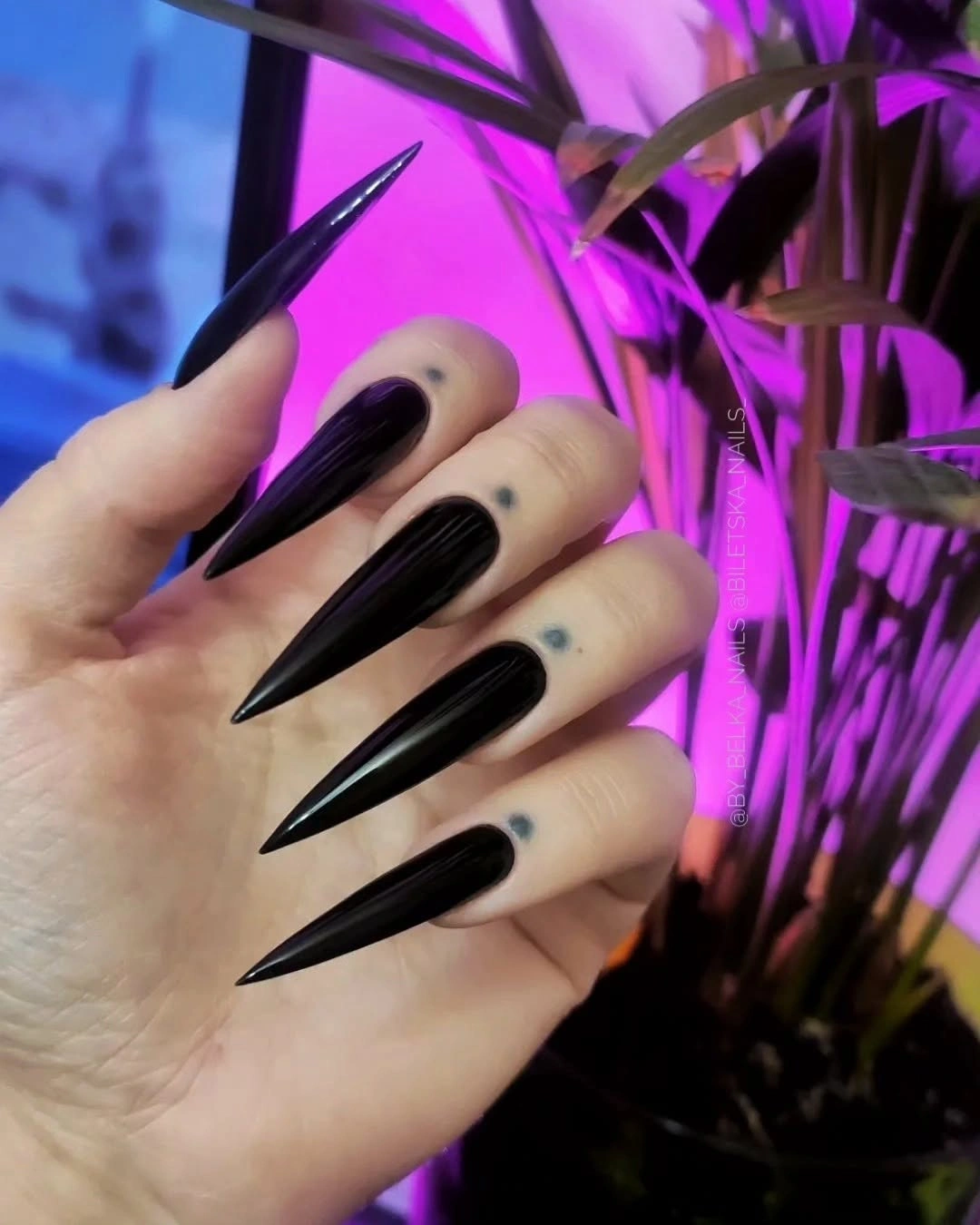 Very long glossy black stiletto nails under purple light