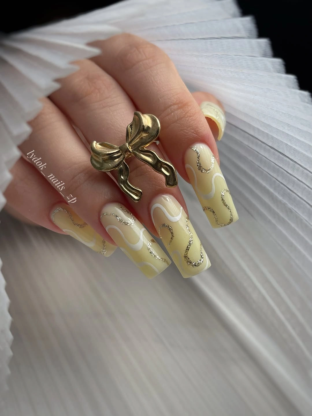 Pale yellow green almond nails with creamy swirls and gold accents