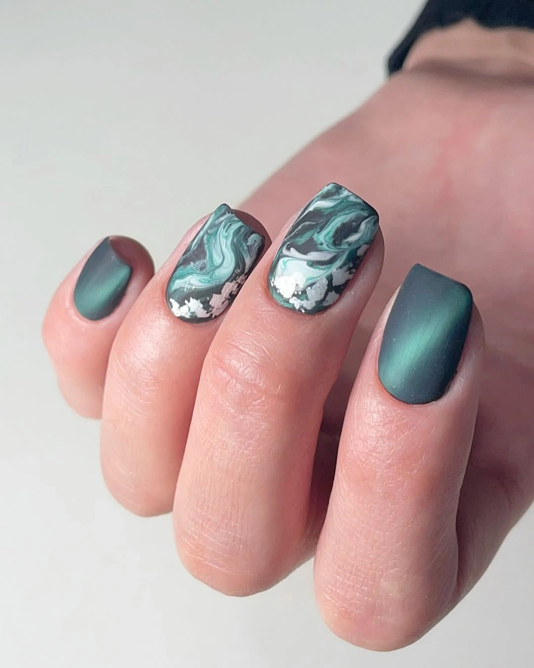 Short rounded teal nails with glossy marbled accents