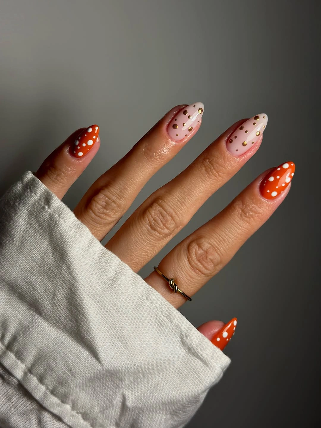 Pale pink almond nails with orange red tips and white dots
