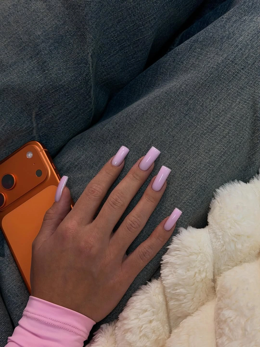 Pastel pink glossy coffin nails resting against denim