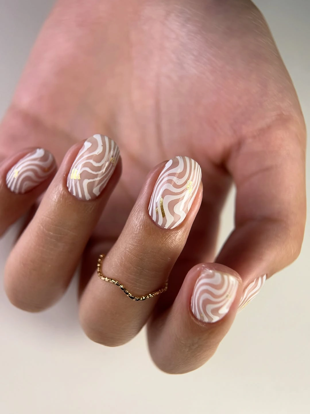 Short nude nails with white wavy lines and gold accents
