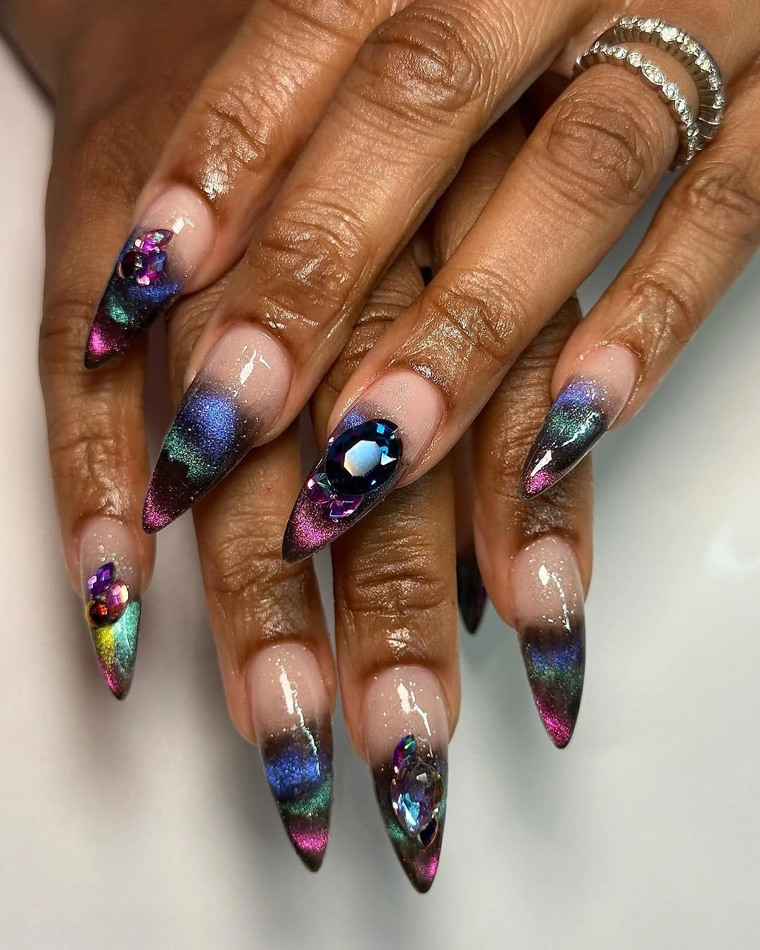 nude stiletto nails with purple blue green jewel accents