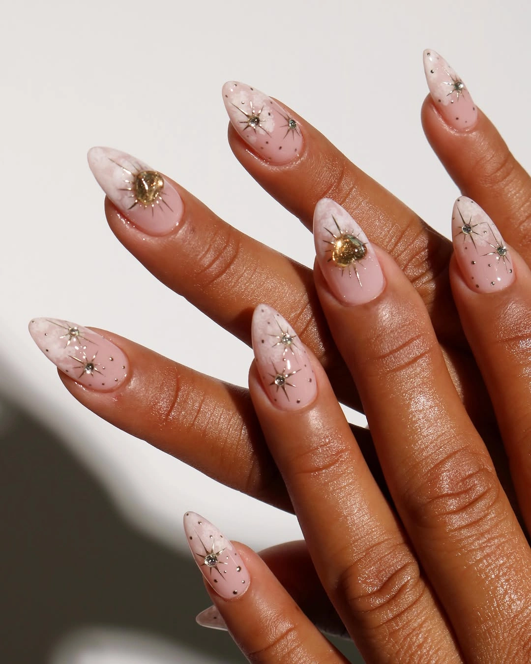 Sheer pink almond nails with speckles and tiny gold accents