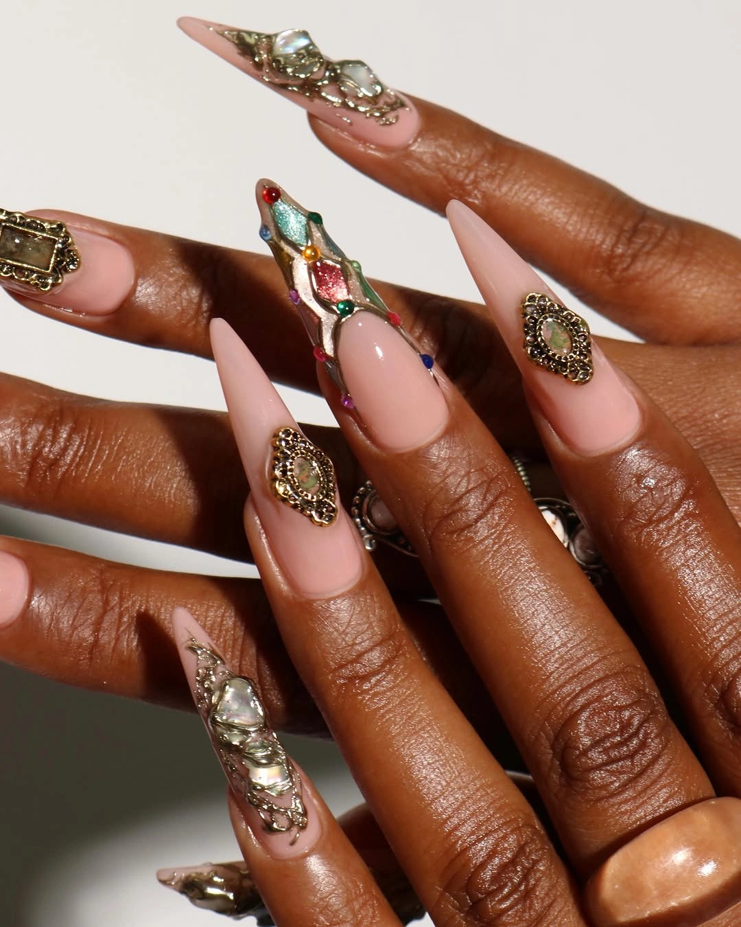 Blush pink stiletto nails with gold ornaments and jewel-like accents