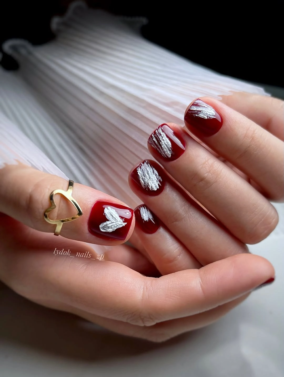 Short glossy red nails with silver accents and a heart