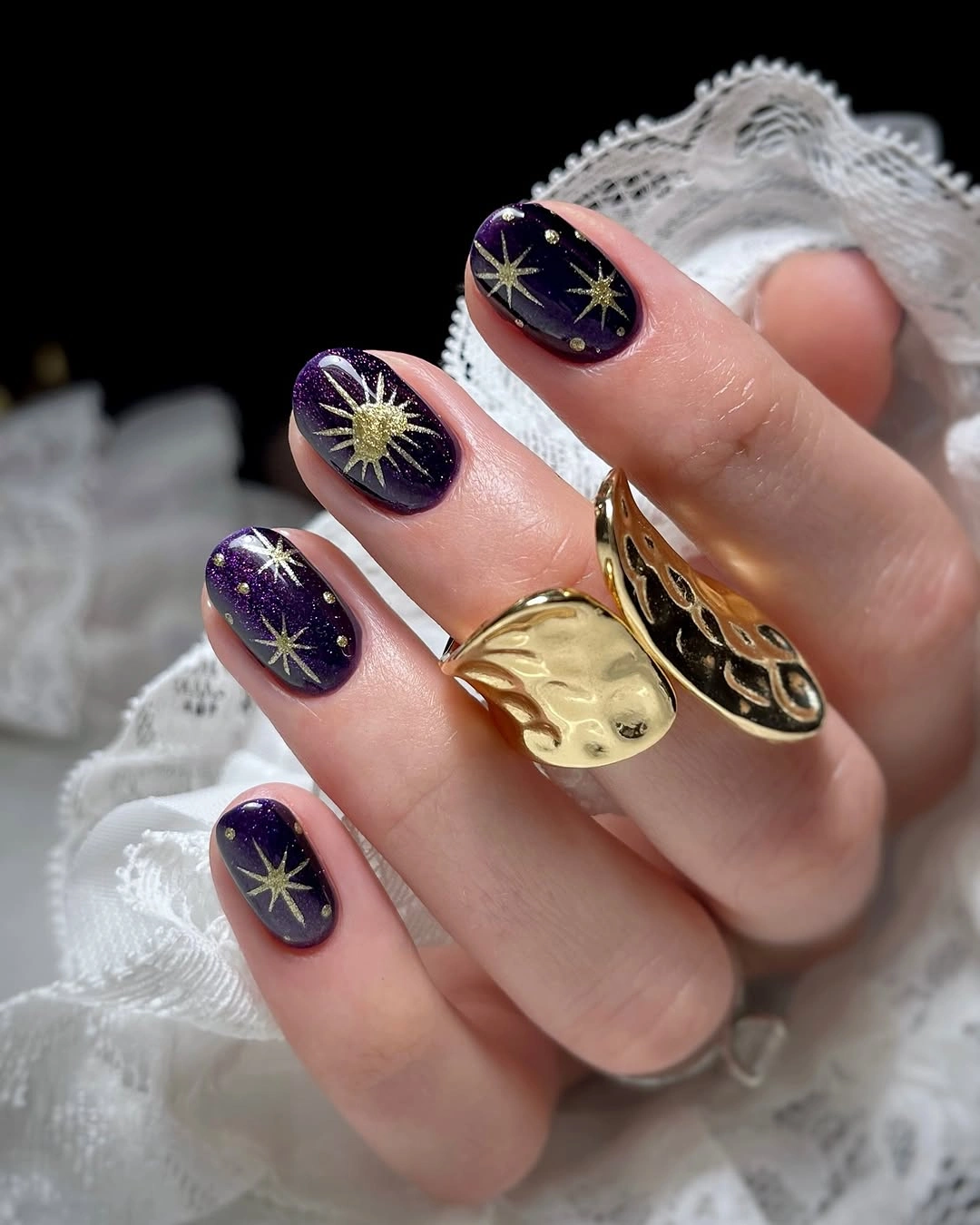 Short dark purple nails with fine gold starbursts