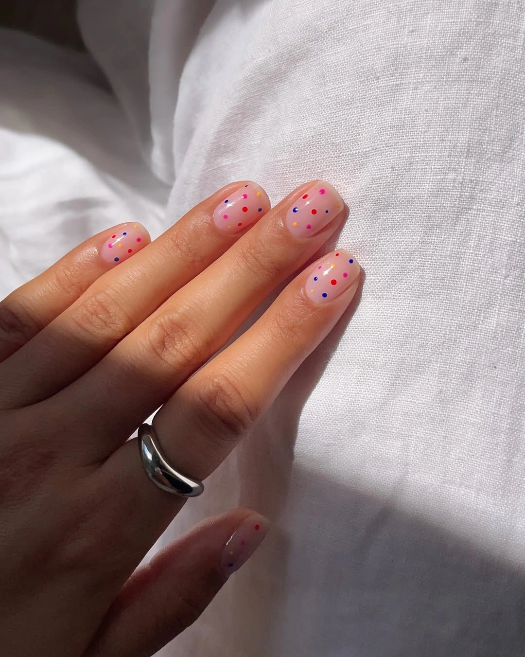 Short pink nails with small red blue and dark dots