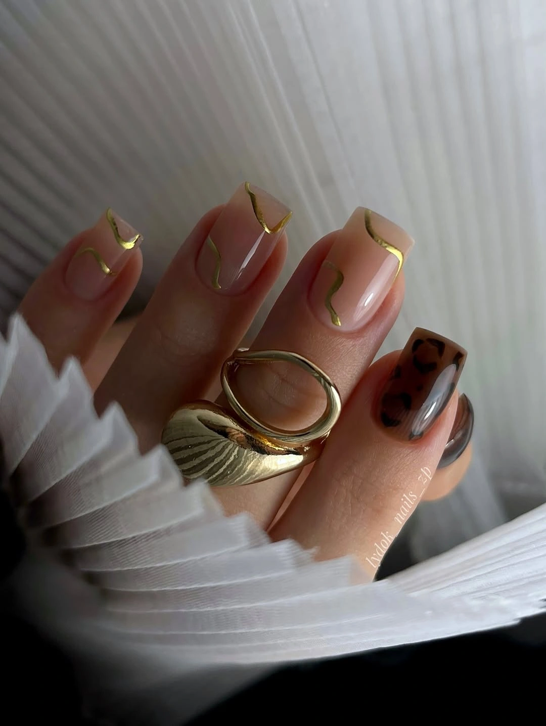 Short almond nude nails with gold tip outlines and brown accent