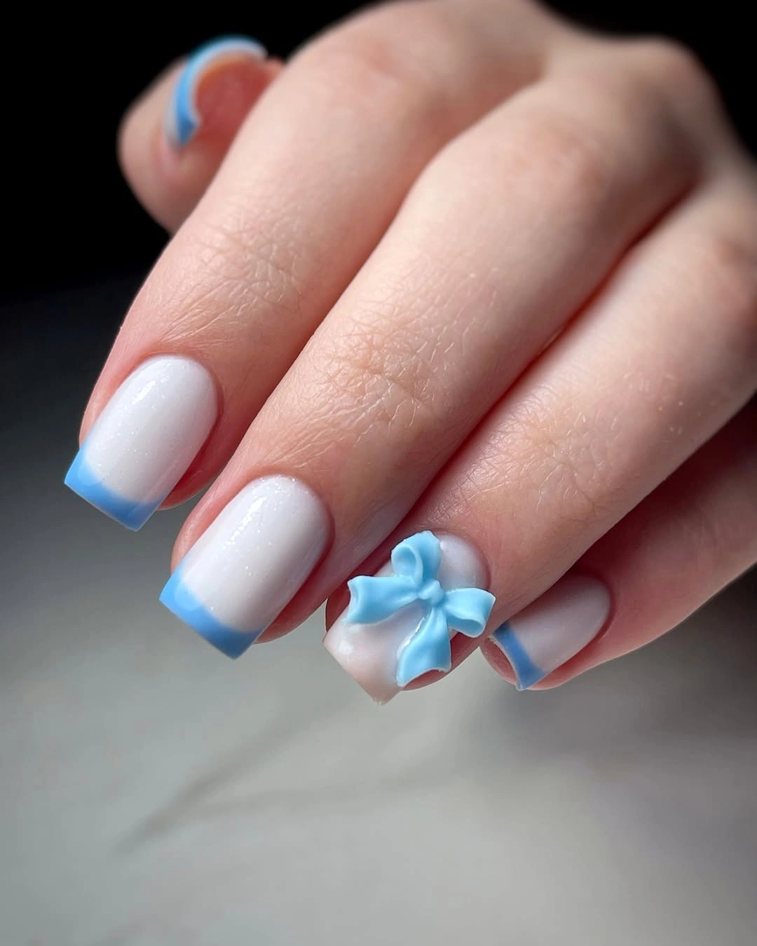 Short white nails with blue French tips and a bow accent