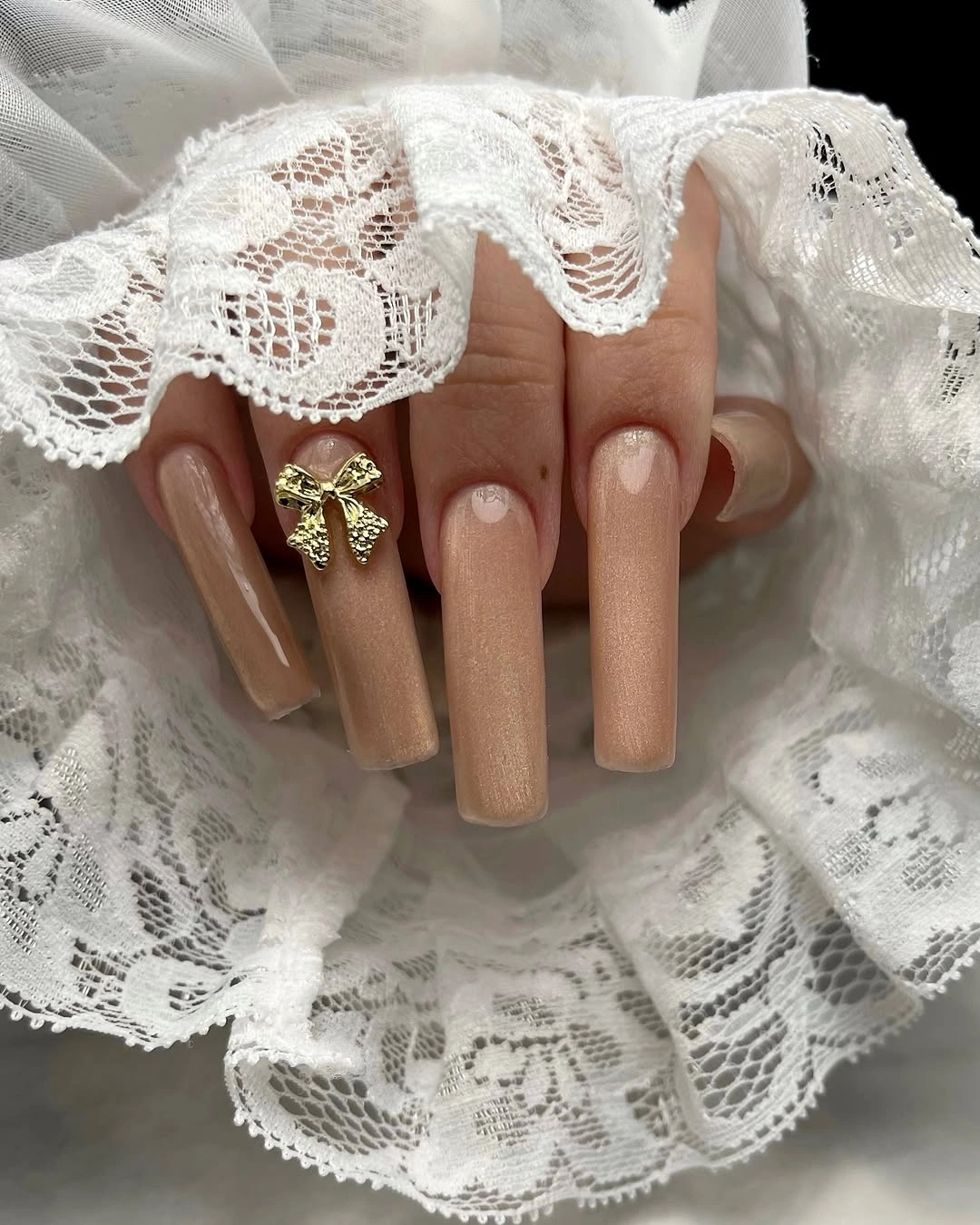 Long nude square nails with gold shimmer and bow charm