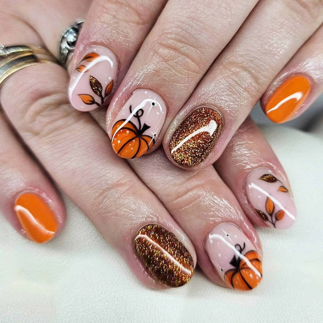 Orange rounded nails with brown glitter and pale pumpkin art