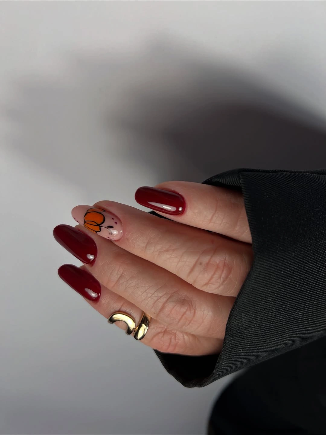 Glossy burgundy almond nails with a tiny pumpkin accent