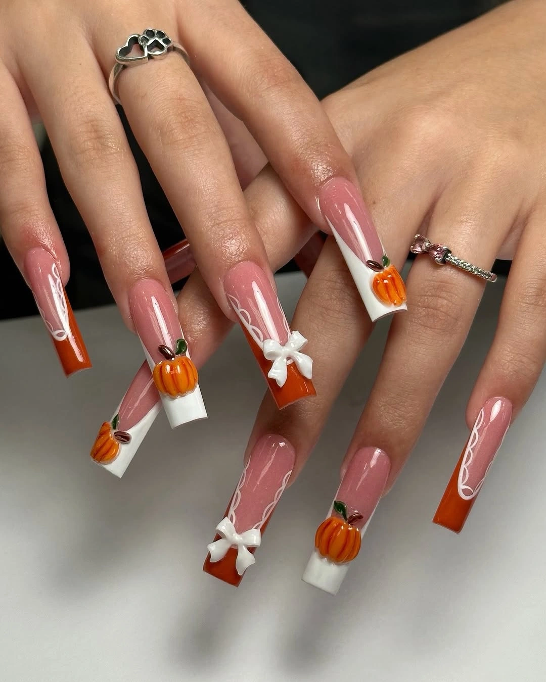 Long pink coffin nails with pumpkin tips and white bows