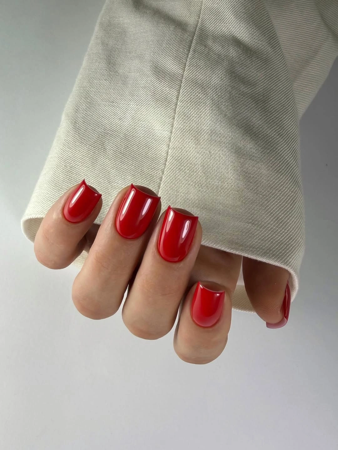 Glossy red square nails beside cream fabric