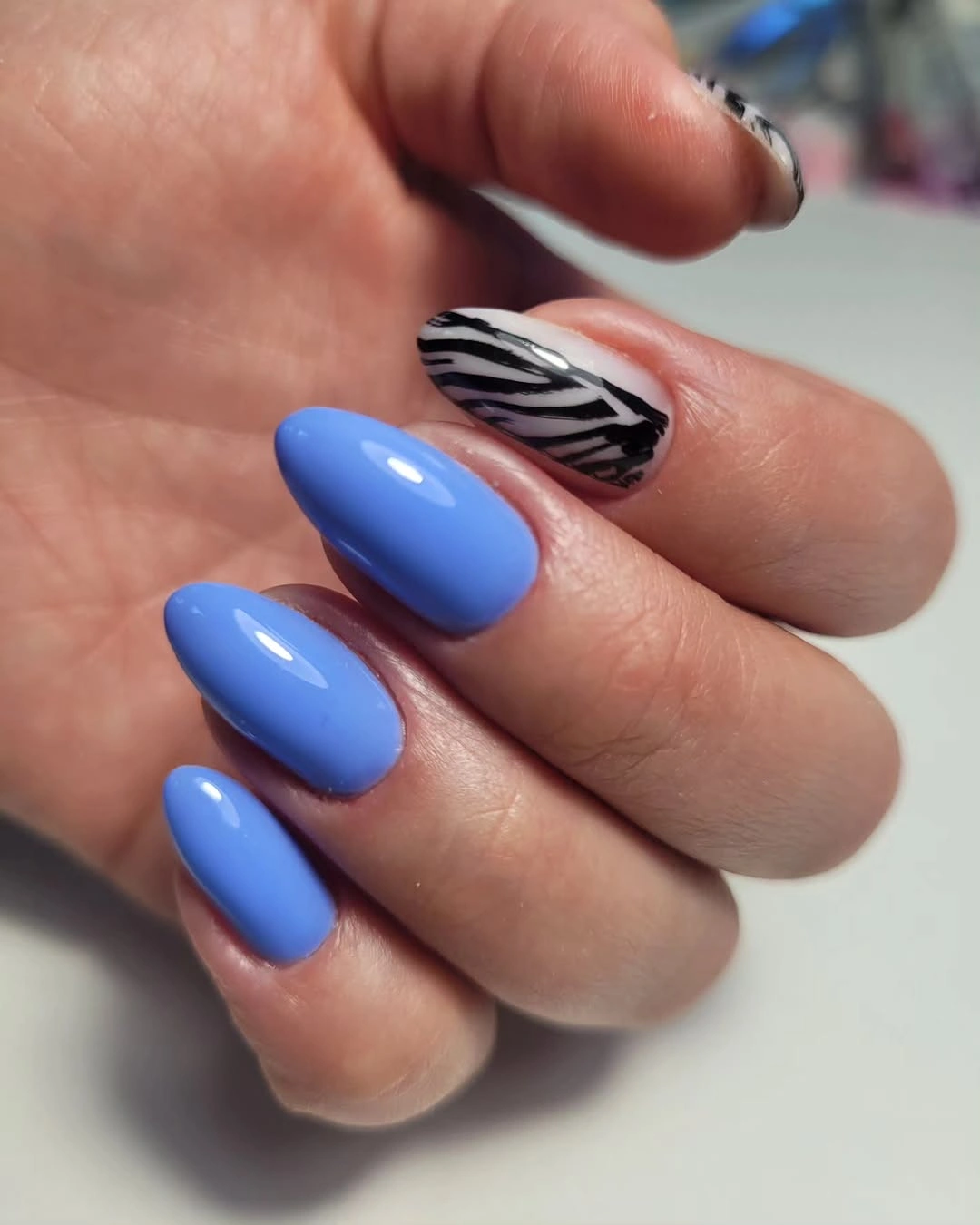 Bright blue almond nails with one black white striped accent