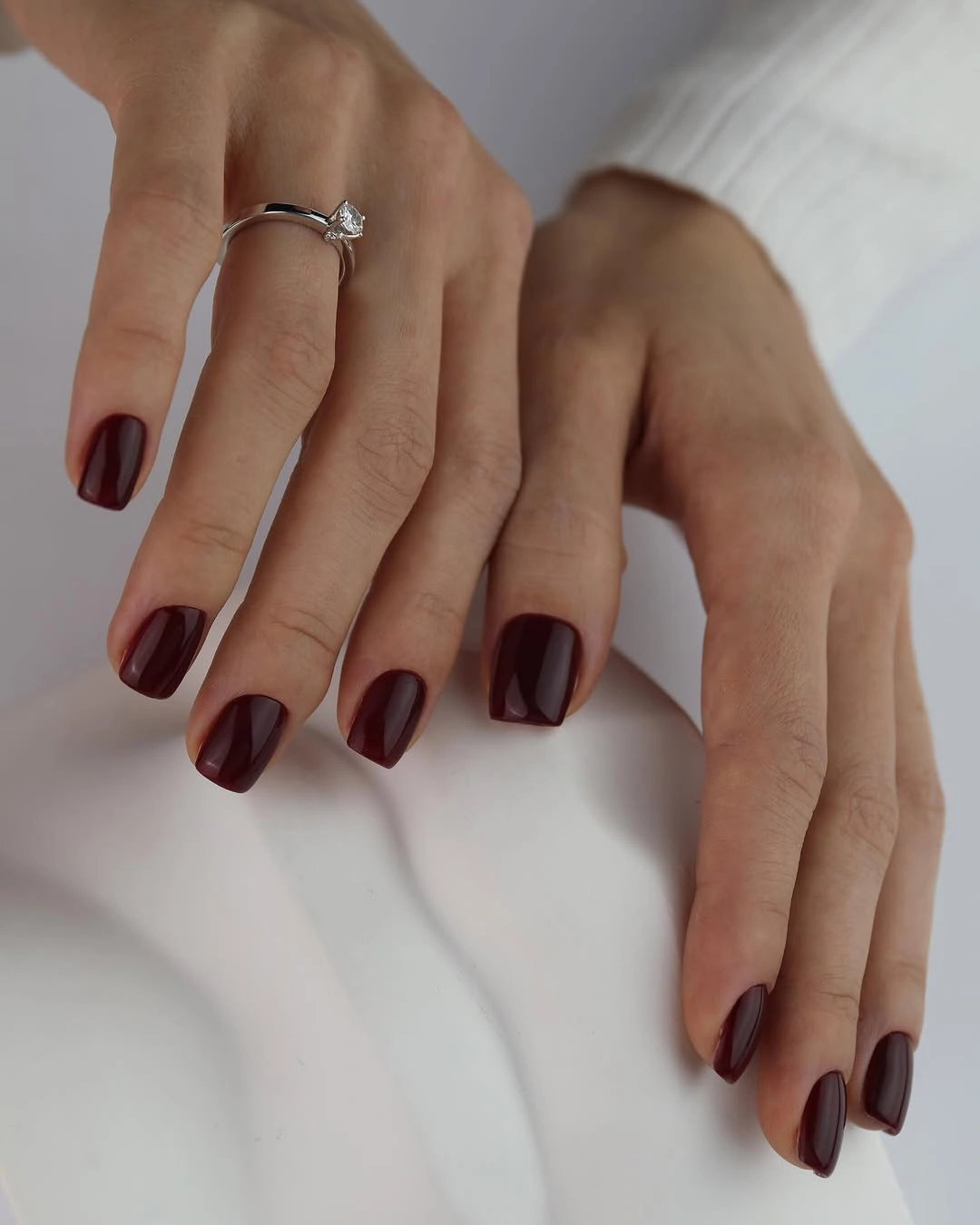 Short glossy burgundy nails shown across both hands