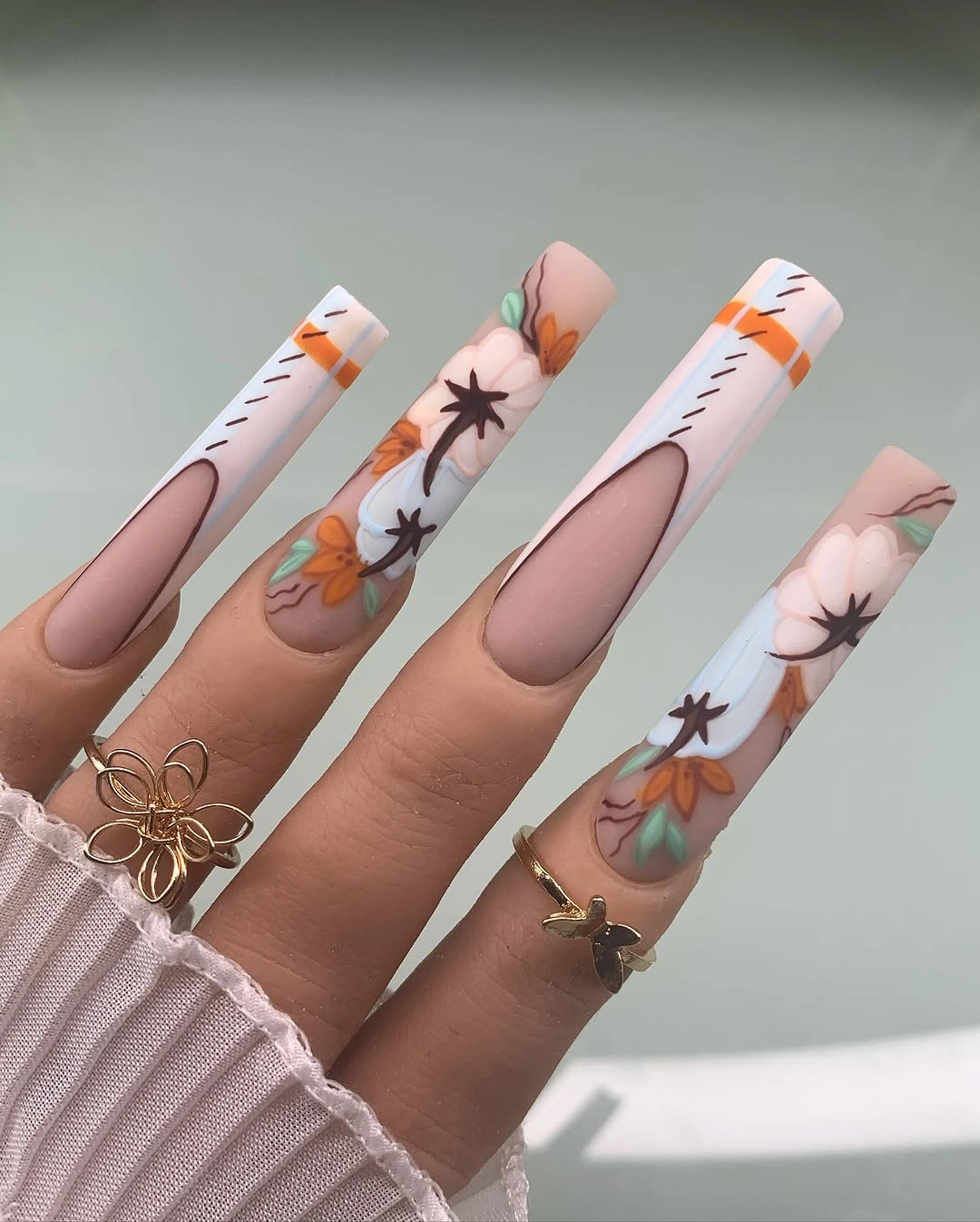 Long soft pink nails with white tips, black spiders, and orange accents