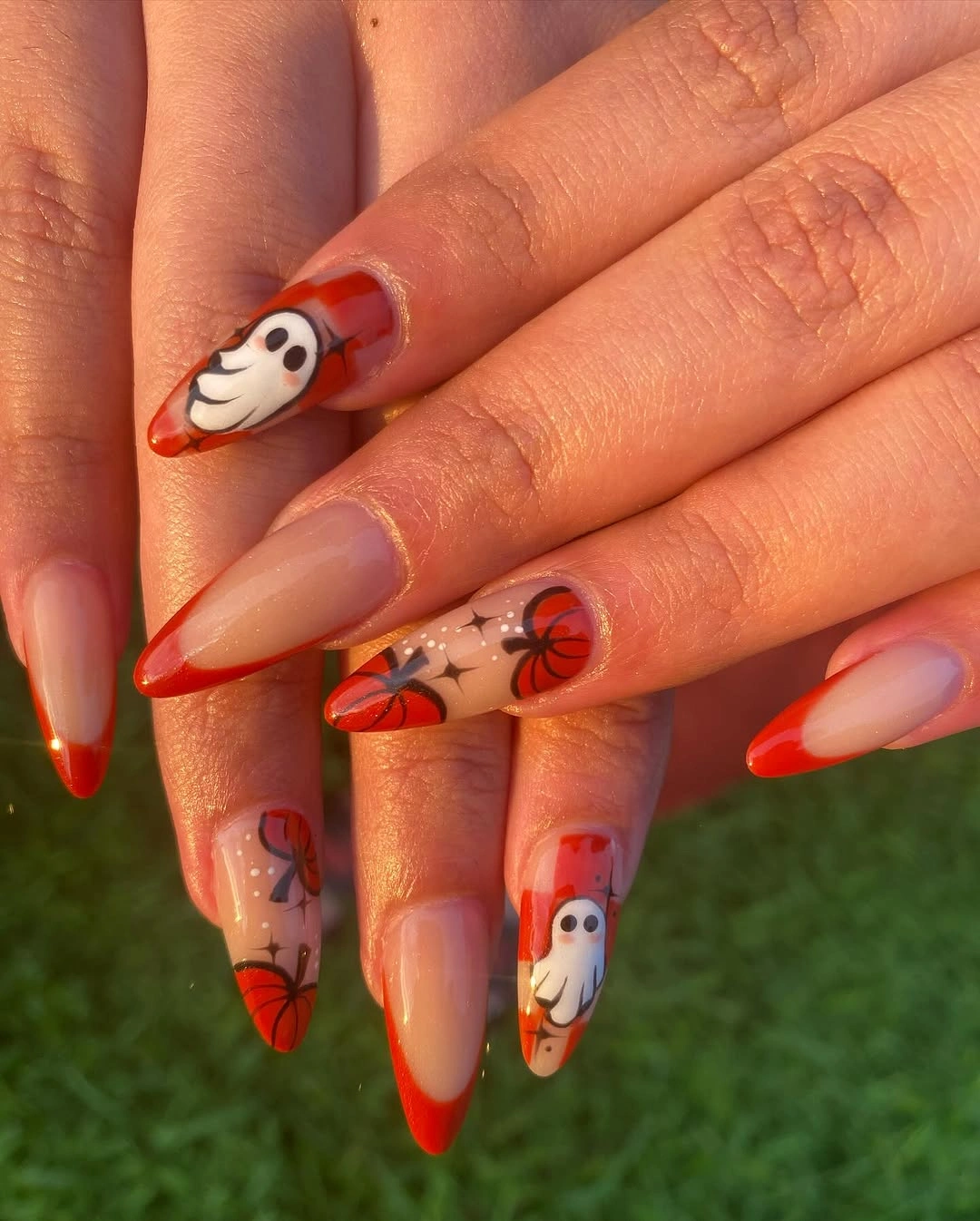 Long nude almond nails with orange curved tips, pumpkin, ghost, and web accents