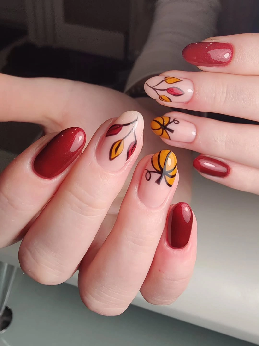 Deep red almond nails with nude accents, black spider, pumpkin, and orange line work