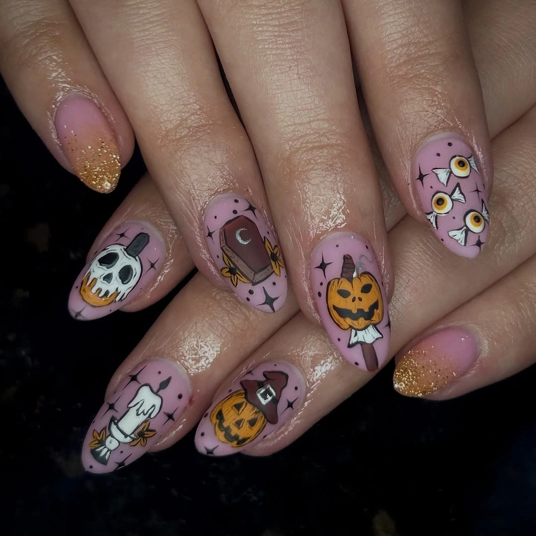 Dusty pink almond nails with black cat, skull, pumpkin, and gold glitter accents