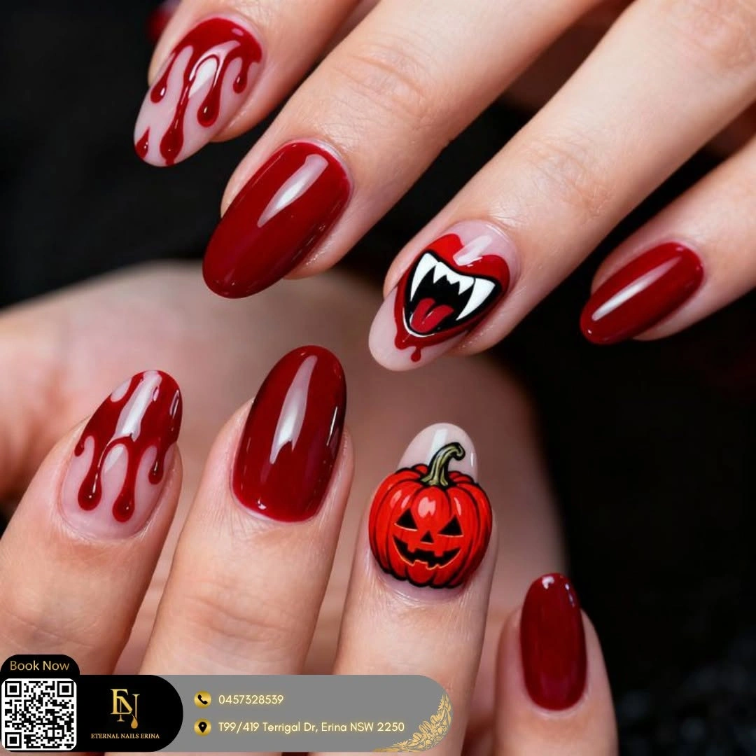Glossy oxblood almond nails with white drips, fanged mouth, and pumpkin