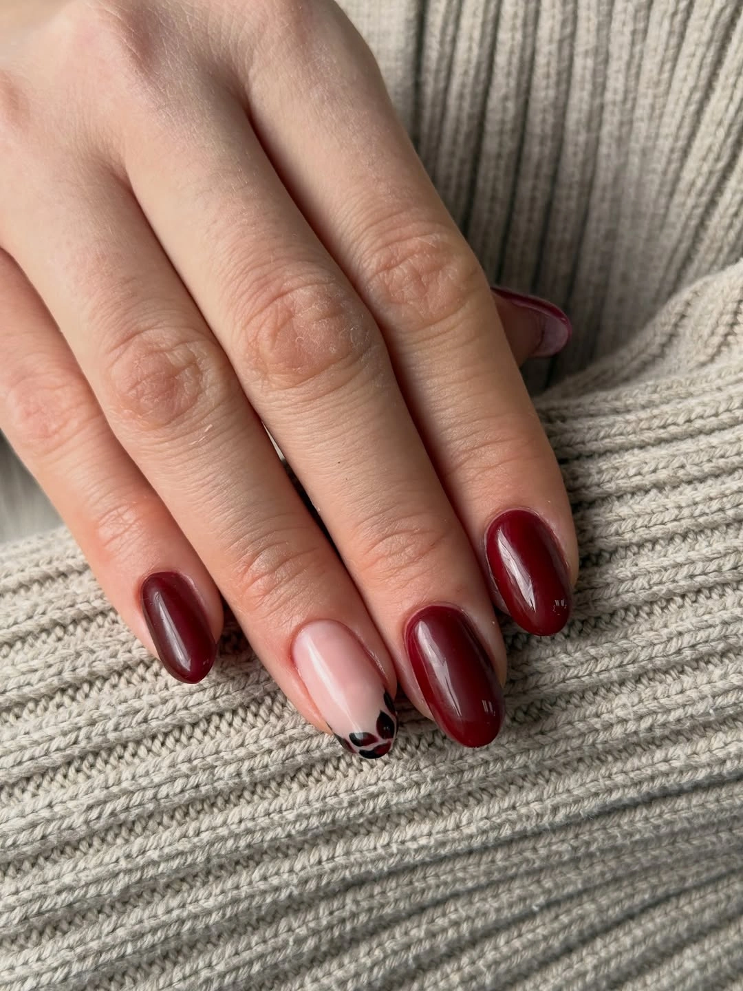 Glossy burgundy nails with one pale nude dark-patterned accent nail