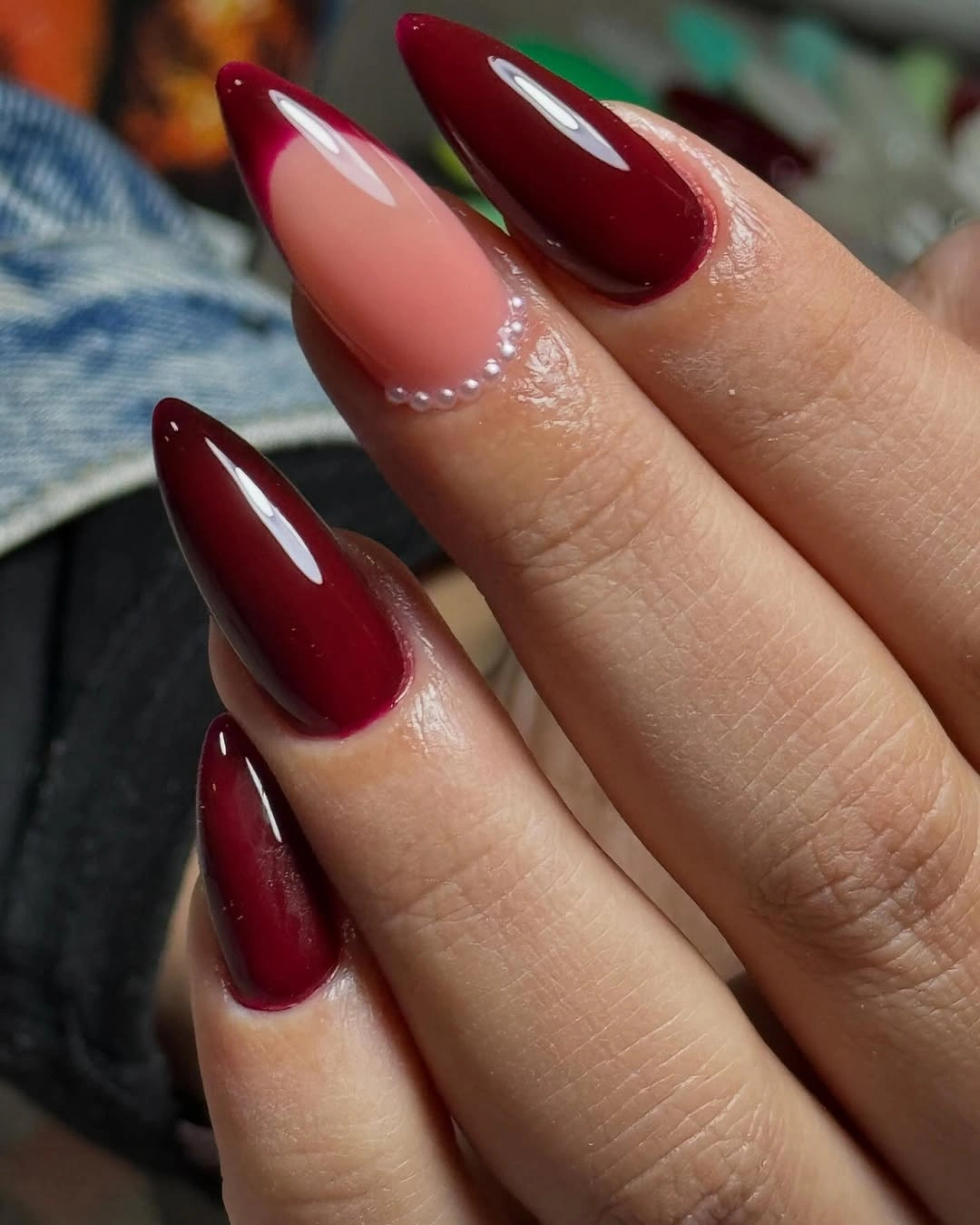 Long maroon and nude almond nails with tiny pearl-like cuticle accents