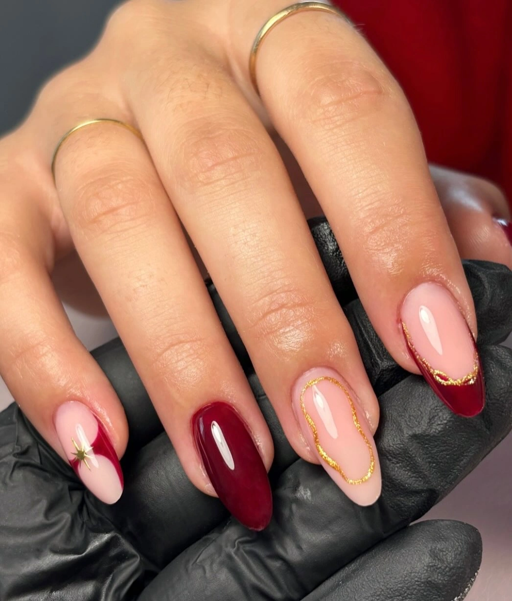 Almond nails with nude base burgundy diagonal sections and fine gold lines