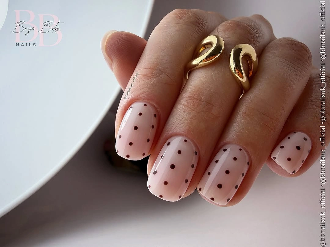 Short soft pink rounded nails with small black polka-dot contrast
