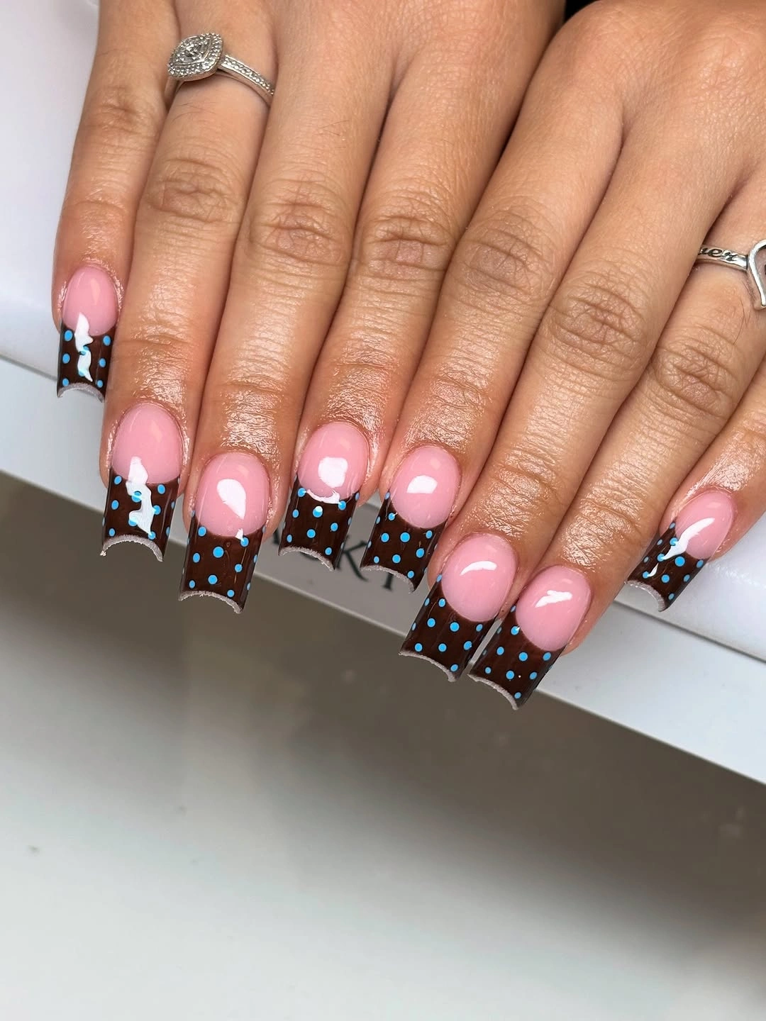 Pink square nails with chocolate dotted French tips and bright blue dots