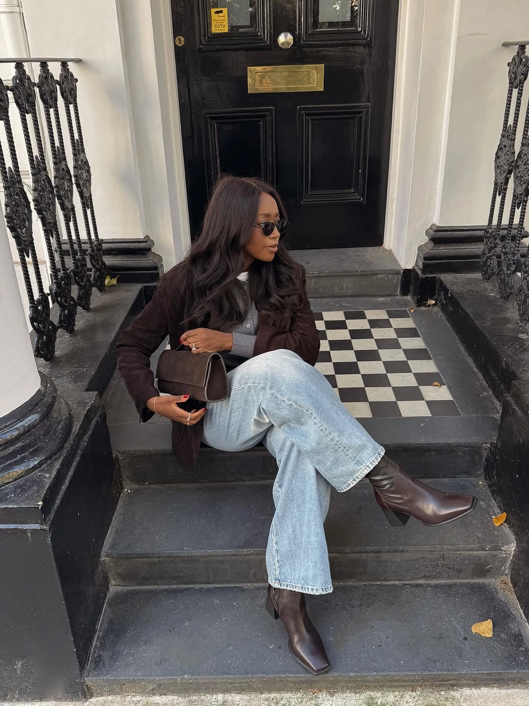 Brown jacket, black top, wide light jeans, and pointed boots