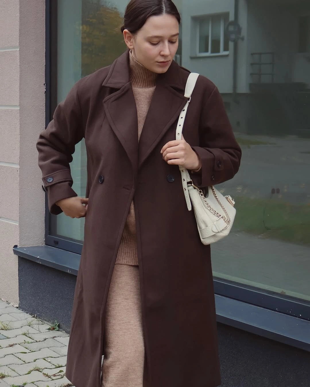 Long brown coat over beige knit column with pale bag