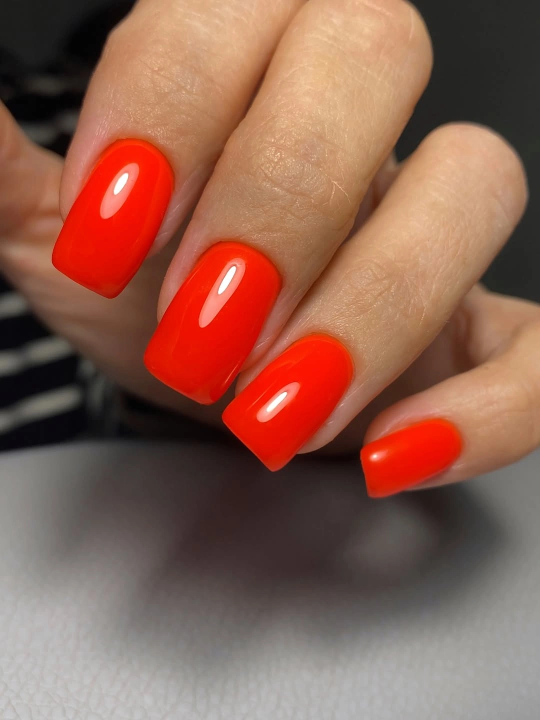 Short square nails in a high-shine orange red color