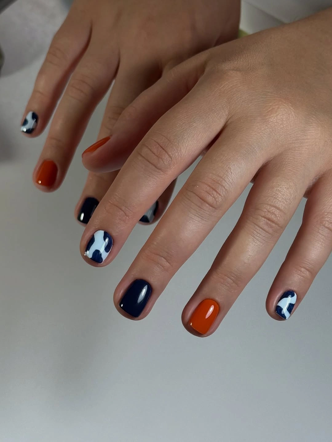 Short orange and navy nails with small white abstract accents