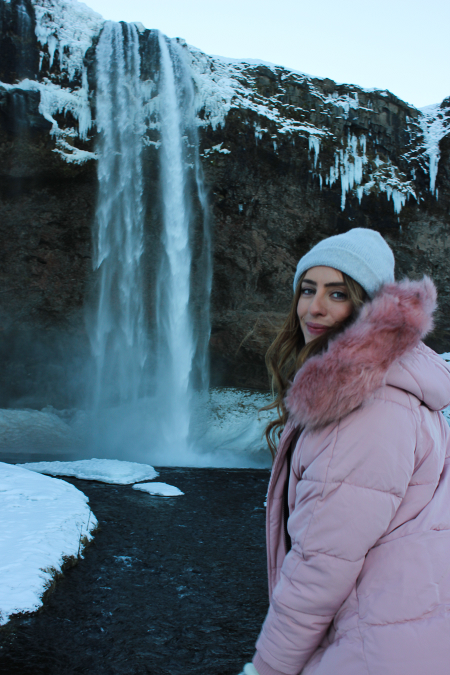 Pink Puffer Jacket with Fur Trim and Grey Beanie by an Icy Waterfall Pink Puffer Jacket with Fur Trim and Grey Beanie by an Icy Waterfall — Iceland Winter Outfits