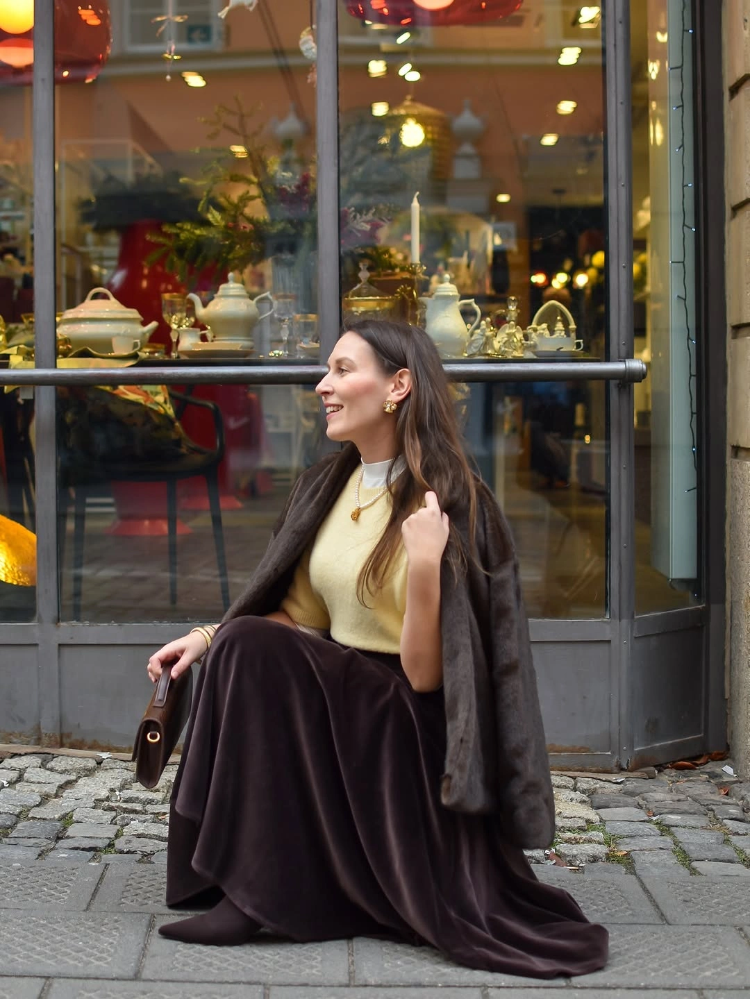Pale top and long dark skirt beside warm shop window