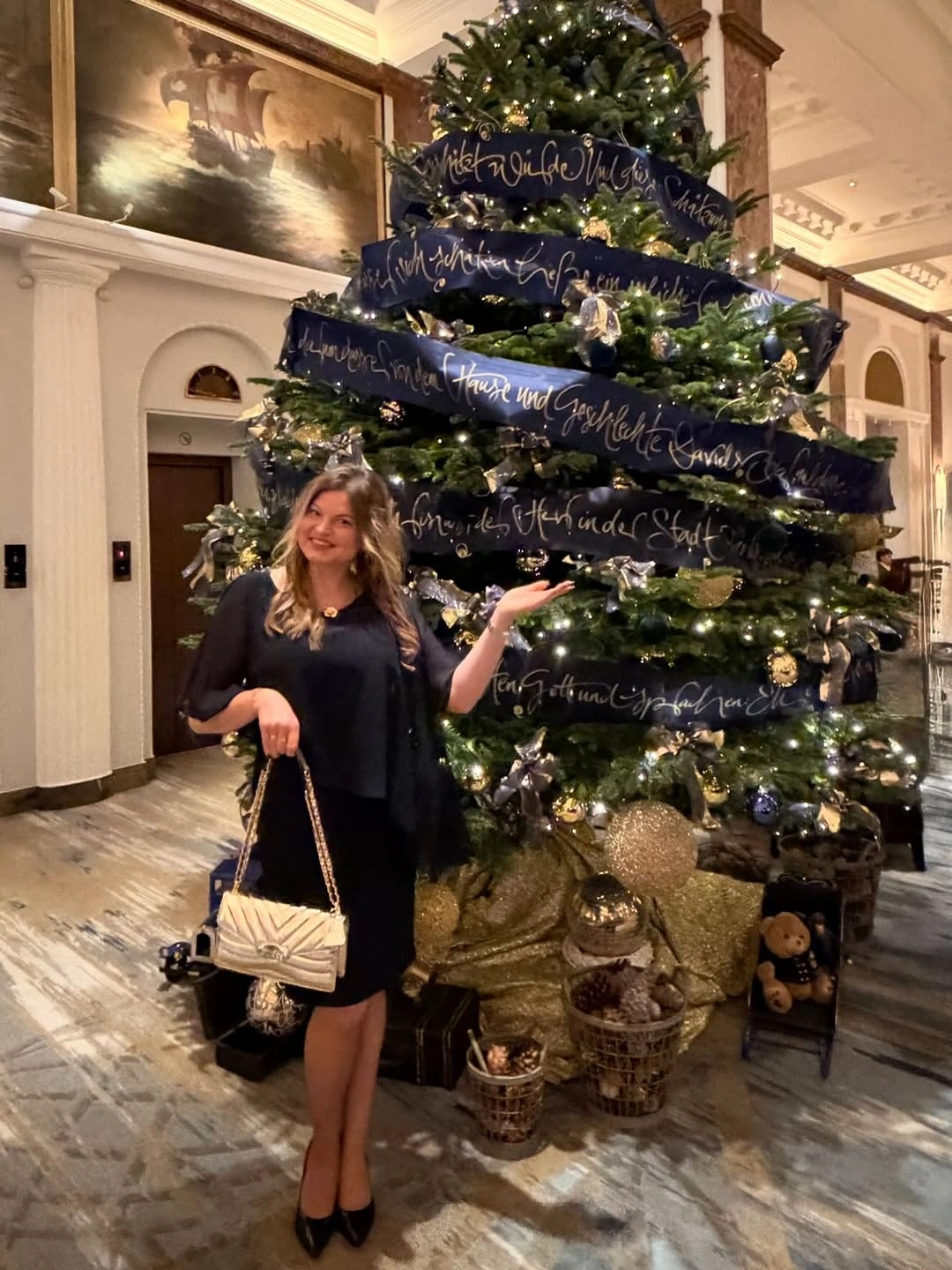 Black outfit with light handbag beside decorated indoor Christmas tree