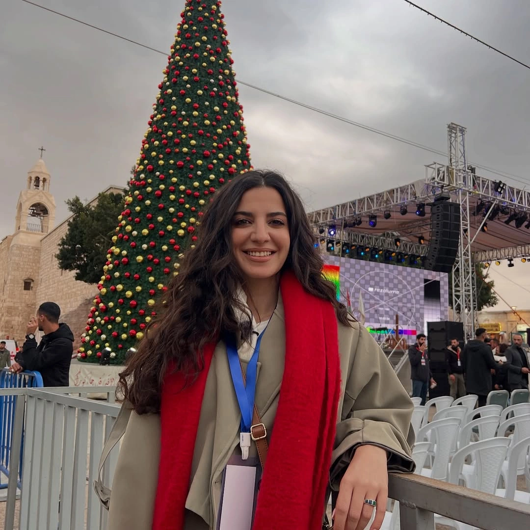 Red scarf over neutral coat beside outdoor Christmas tree