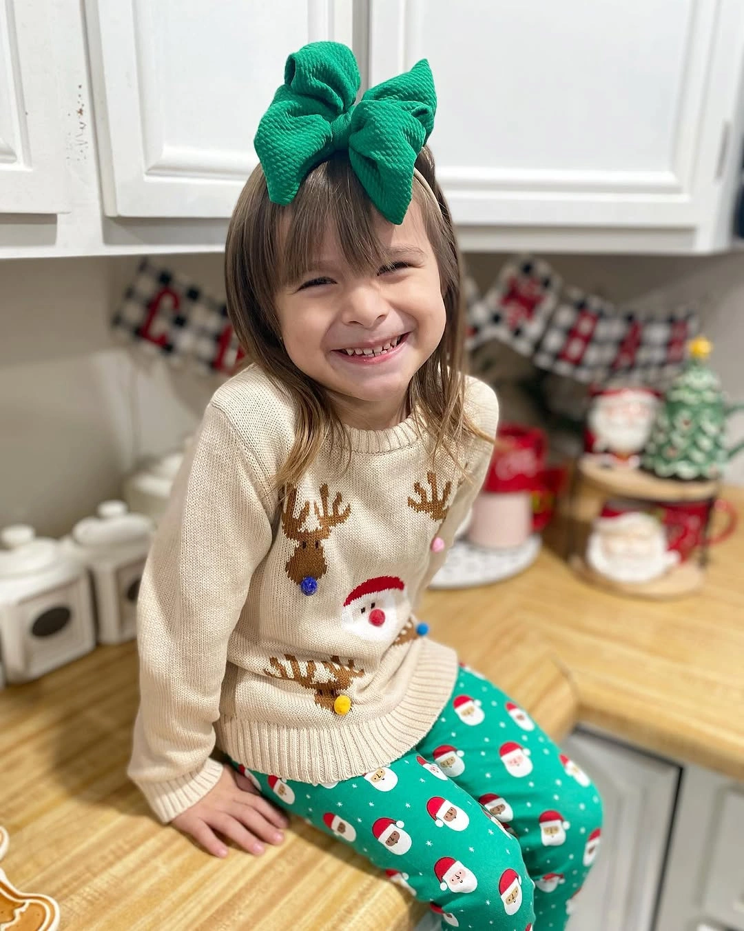 Child in cream Christmas sweater green printed pants and bow