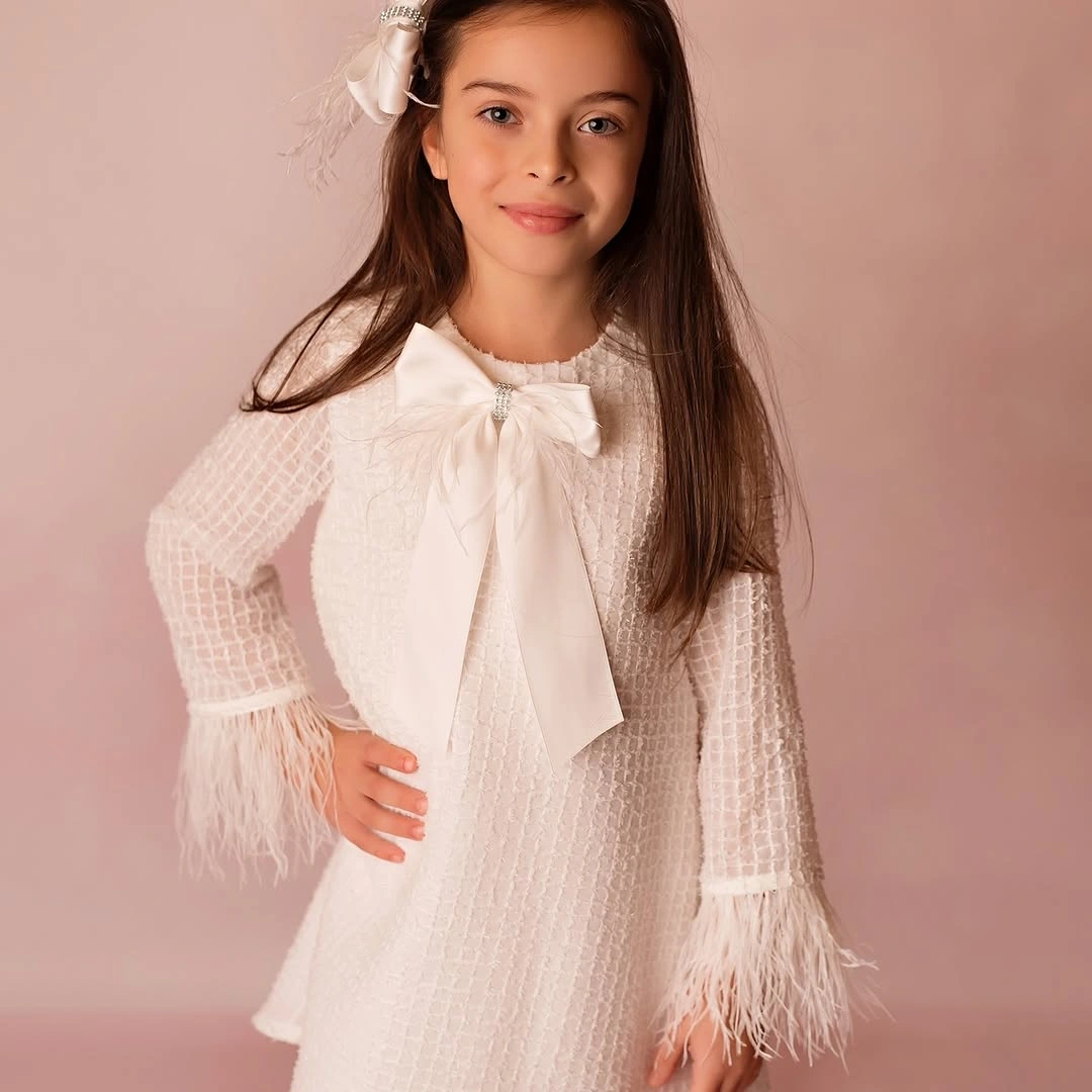 Child wearing white dress with large bow and textured sleeves